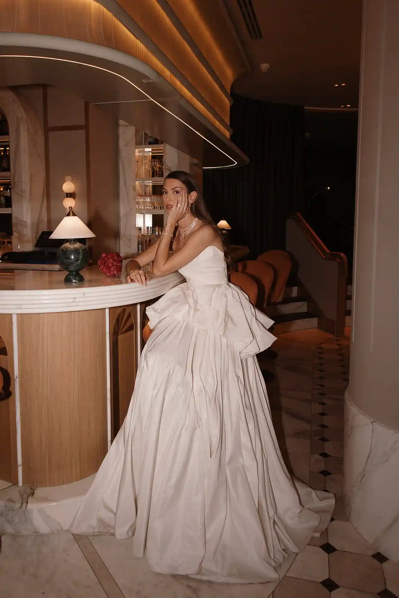 Woman in a white dress sitting at a bar counter in an elegant interior setting.