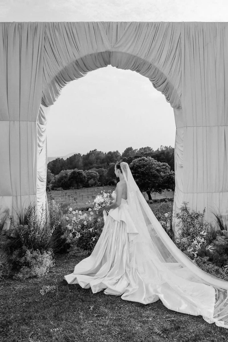 Bride standing under a draped archway with a scenic background