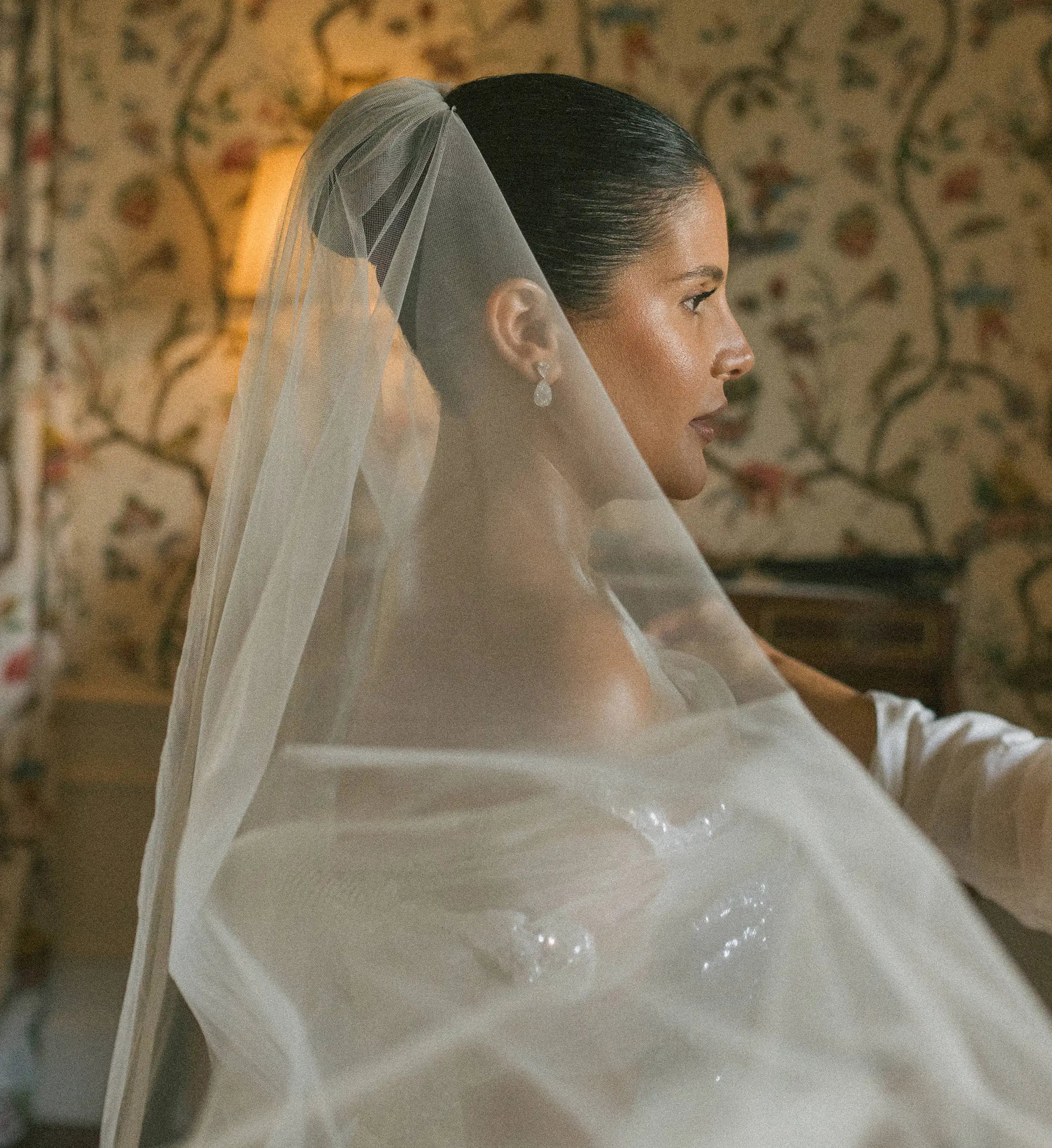 Woman wearing a veil in a room with floral wallpaper