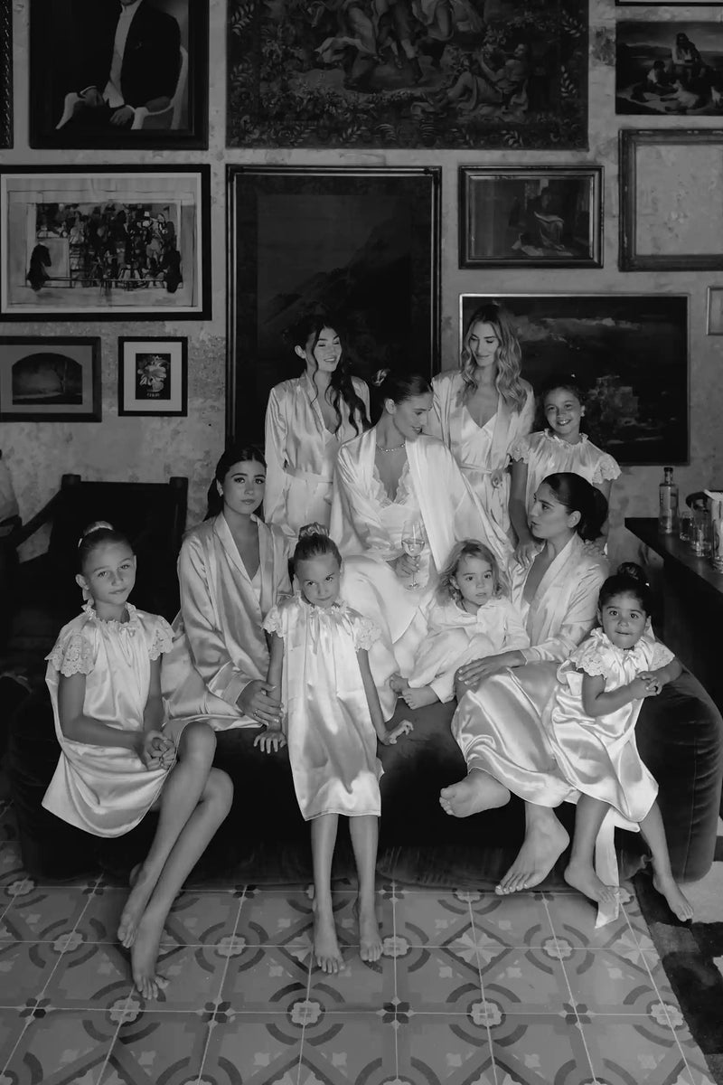 Group of women and children in formal attire sitting together in a room with framed pictures on the wall.