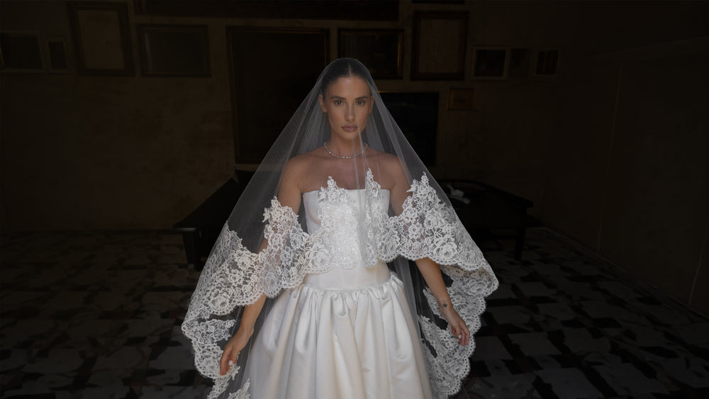 Woman in a white wedding dress with a veil in a dimly lit room.