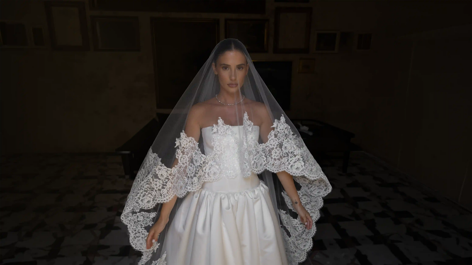 Woman wearing a white wedding dress with lace details in a dimly lit room.